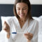 A smiling woman holding a pregnancy test stick.