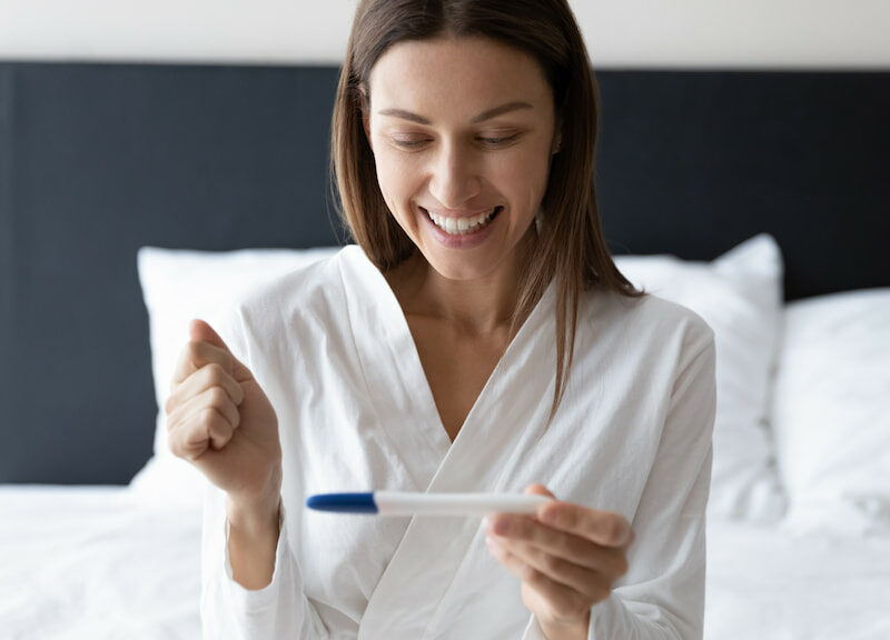 A smiling woman holding a pregnancy test stick.