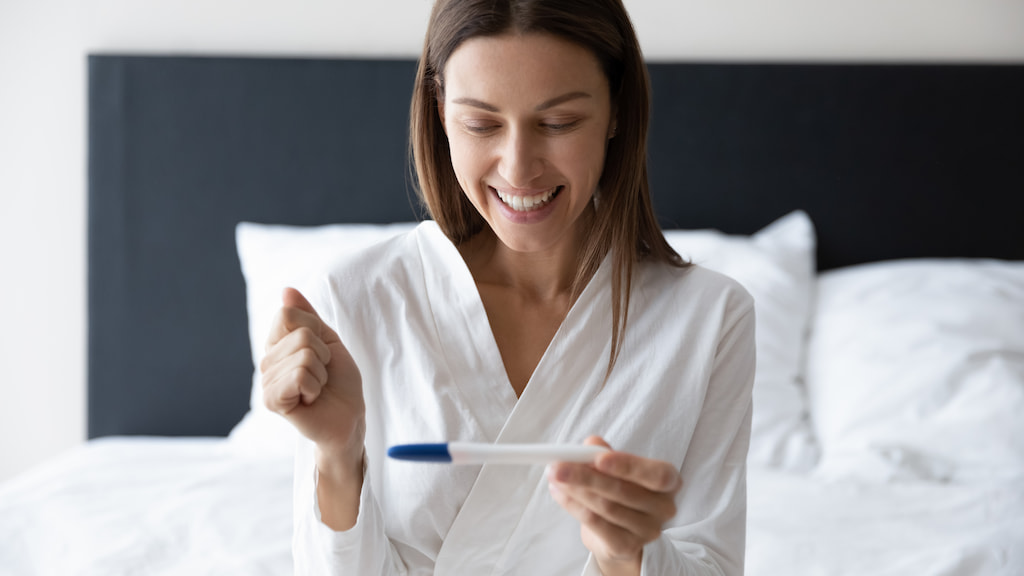 A smiling woman holding a pregnancy test stick.